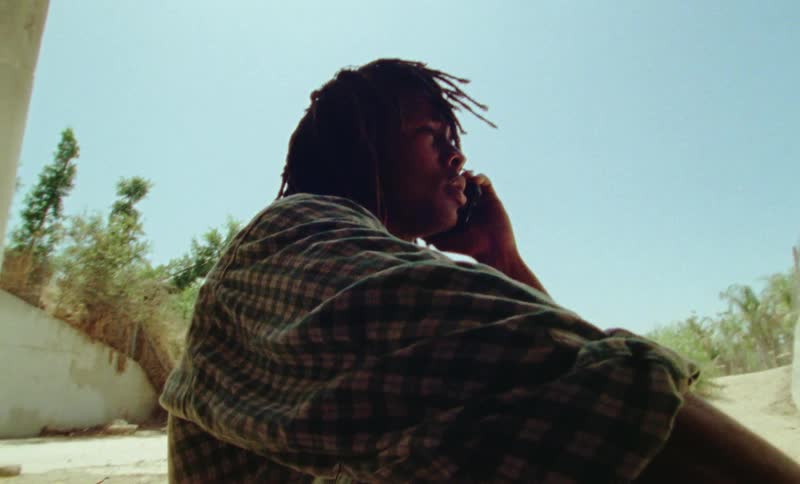 Man sitting in the ground in the shadow of a structure talking on the smartphone outdoors