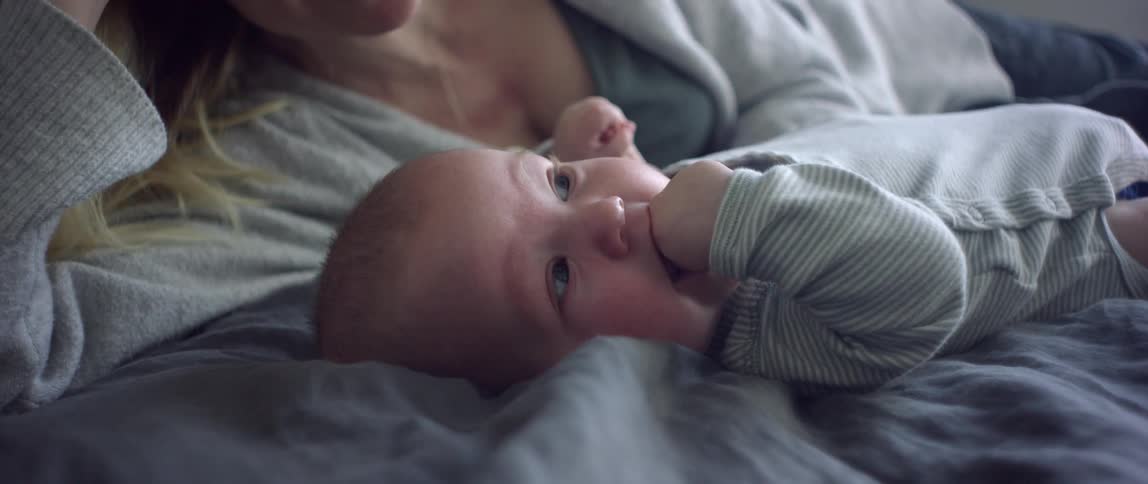 A woman lies on a bed next to her baby