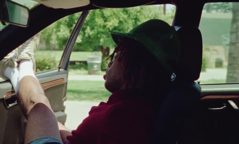 A man naps in a parked vehicle with the door open and his legs resting on the window