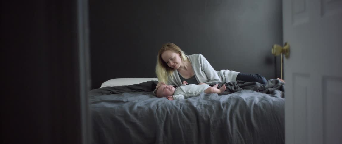 A woman lays on a bed next to a baby