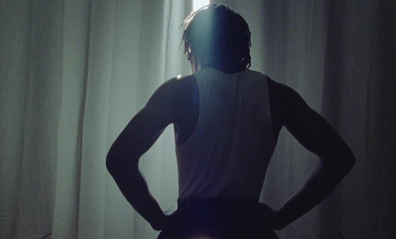 Silhouete of a young fit man wearing a sweatshirt standing in front of a curtain in a dimly lit room
