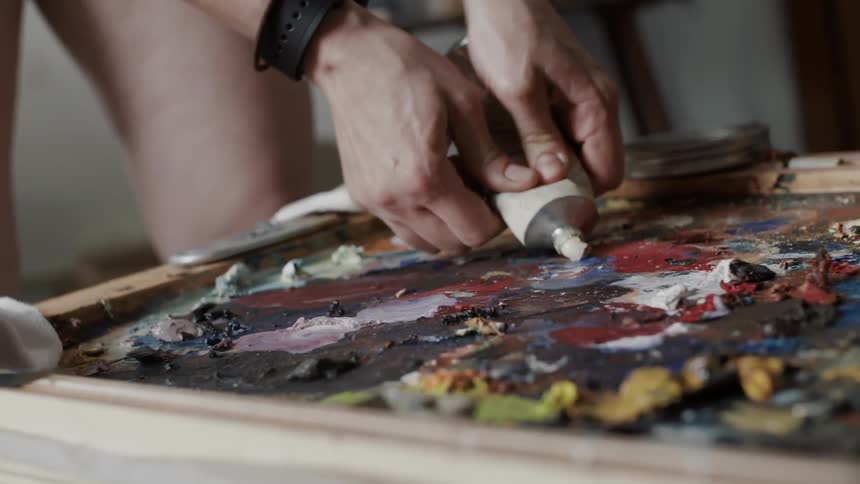 A person squeezes some paint on a board