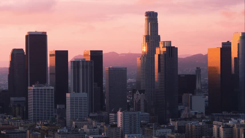 A view of a city with all sizes of buildings against mountains and a pink sky