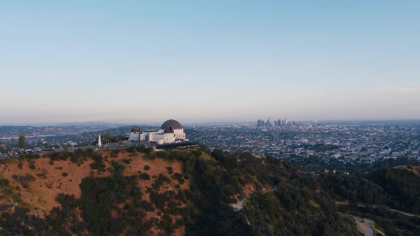 A white building with a dark dome is located on a hilltop overlooking a sprawling city