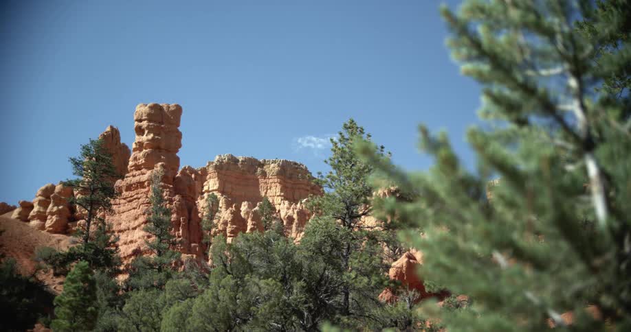 A cliff and canyon with trees in the foreground and the sky and clouds in the background