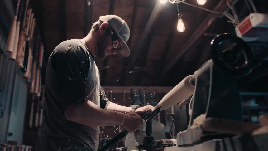 A man is carving a baseball bat on a machine