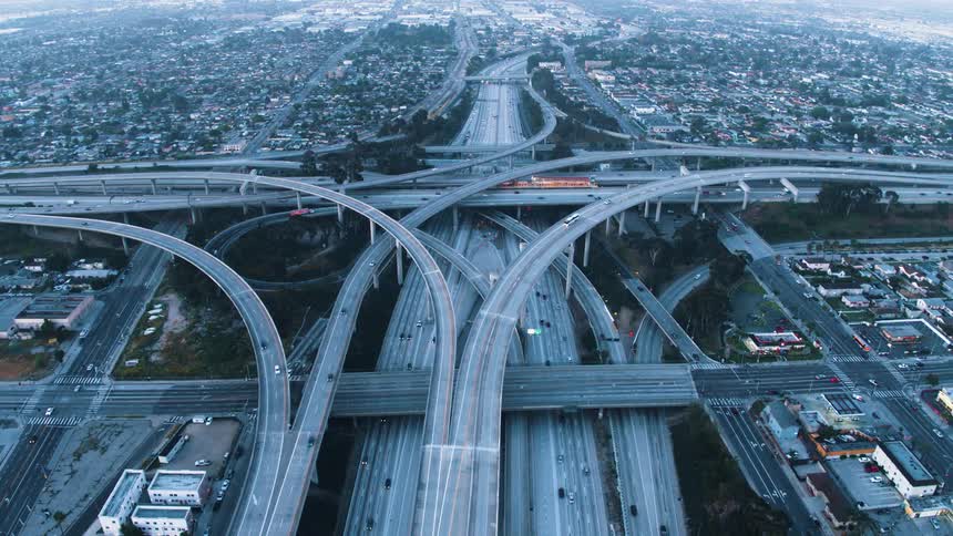 Aerial view of cars driving on a highway through a city is displayed