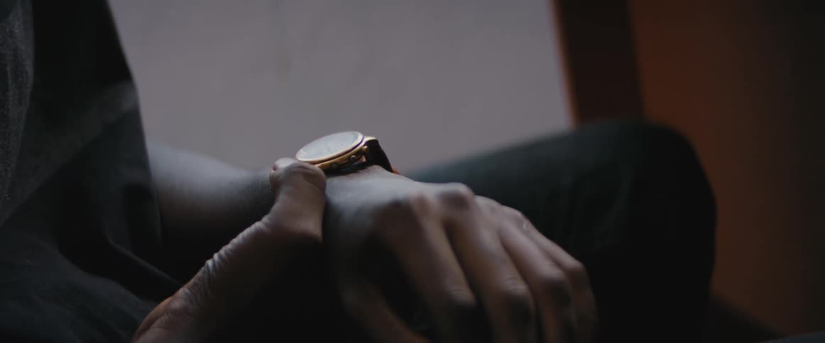 A man sits and touches the face of his wristwatch