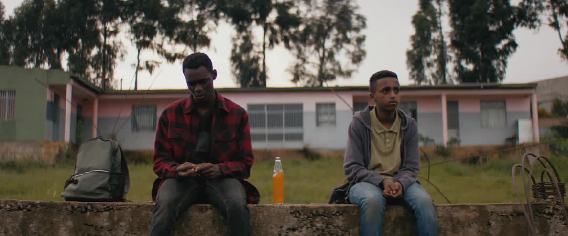 Two males are sitting on a concrete wall in front of a building