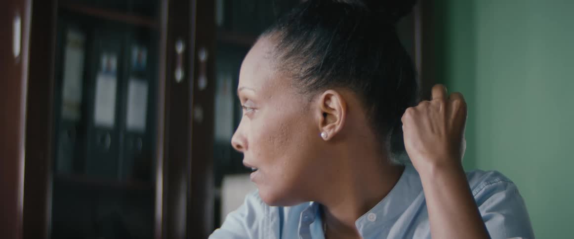 Tired woman sitting in a room looks away and sighs before getting up