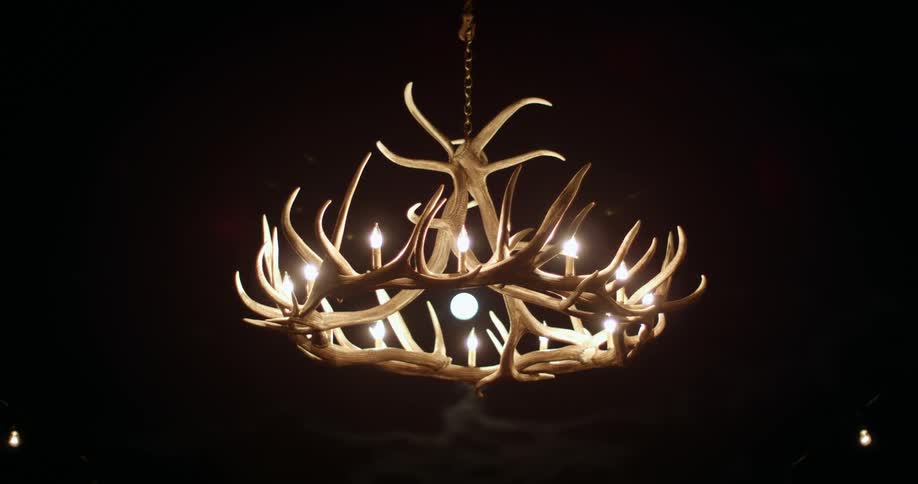 A chandelier made of antlers with light bulbs hanging from a black ceiling
