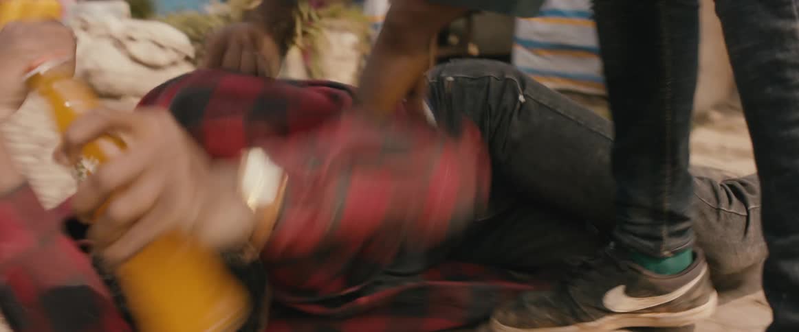 A man lies on the ground and shields his eyes as another man repeatedly kicks him and steals his drink