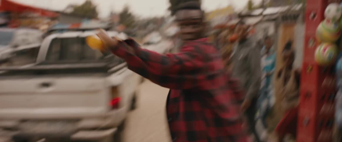 A young man looks behind him as he runs carrying a womans purse through a street lined with shops