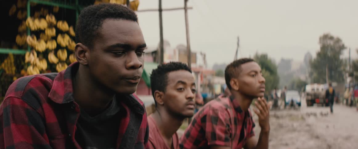 Three men sit on the side of a road intently watching something across from them