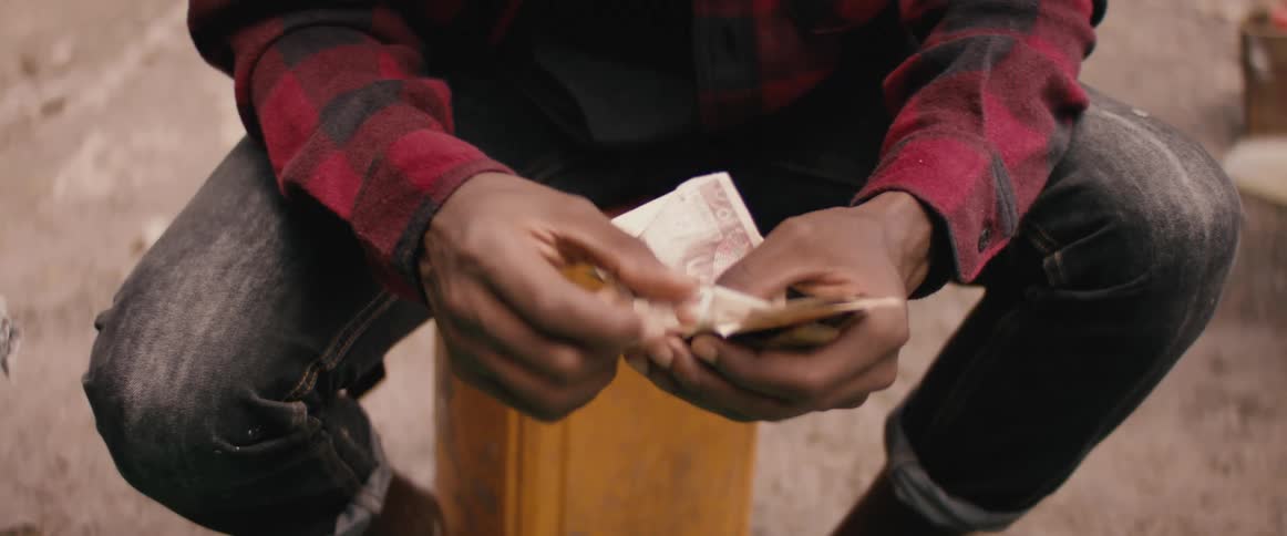 A person with jeans sitting on a box counting money