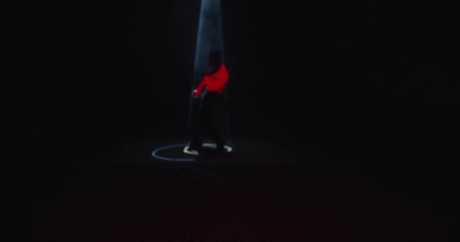 A man wearing a red jacket and black pants raises his arms and dances in a black space illuminated only by strobing lights