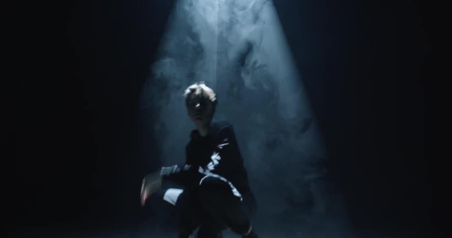 Young man crouching in a dark smoky room under a spotlight
