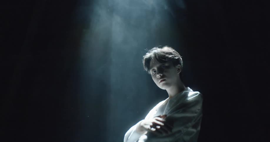 A model pushes up her sleeve as she stands under a smoky spotlight
