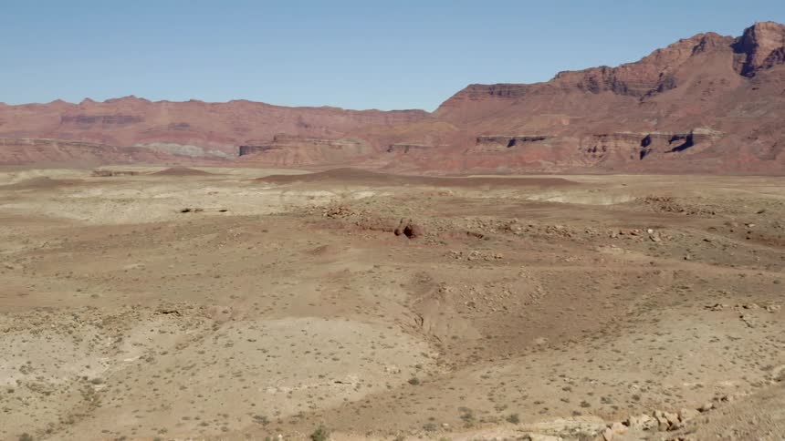 Slopes of light brown sand and rocks next to a red mountain range at daytime