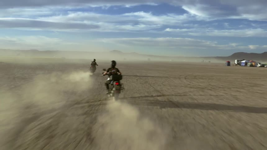 Two people drive motorcycles across a dirt field