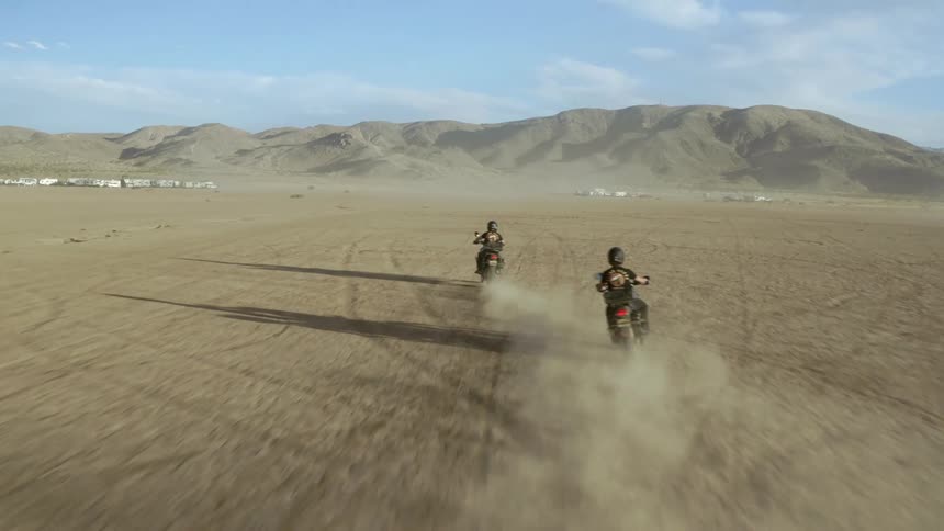 Two cyclists riding dirt bikes across the desert toward the mountains