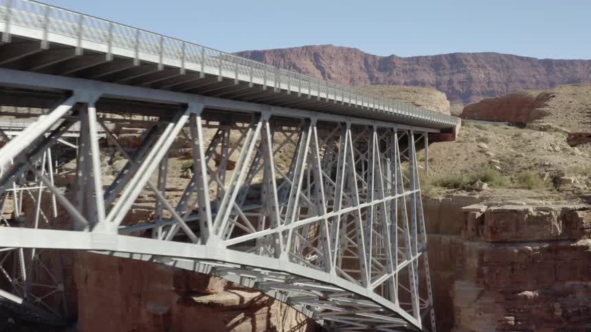 Silver bridge stretching over towards large brown dust covered mountains and plateaus at daytime