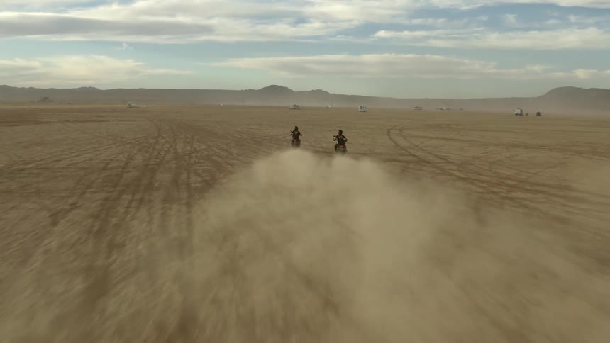 Two motorcycles race across the surface of a dry and dusty desert landscape
