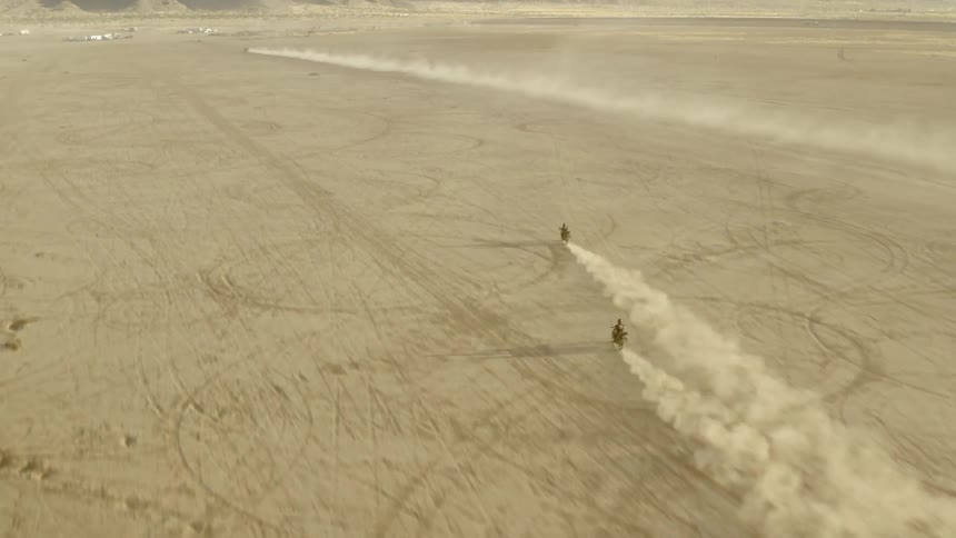 Two cyclist riding dirt bikes across the desert towards a mountain range