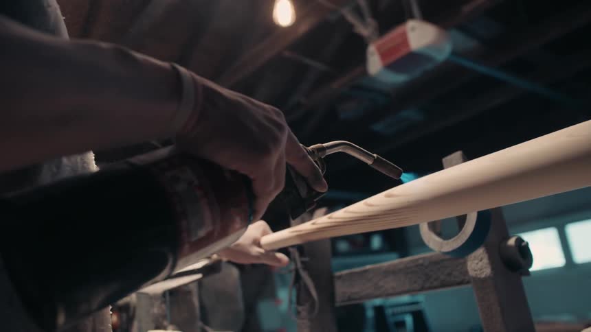 A man uses a blowtorch on the surface of a baseball bat he is making
