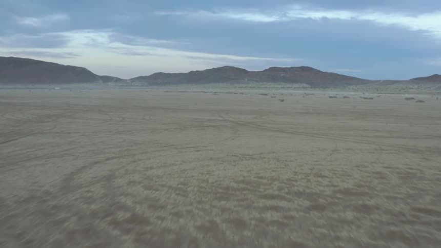 Aerial view of the dirt roads and vehicle tracks over the sand of a desert near the mountains at morning