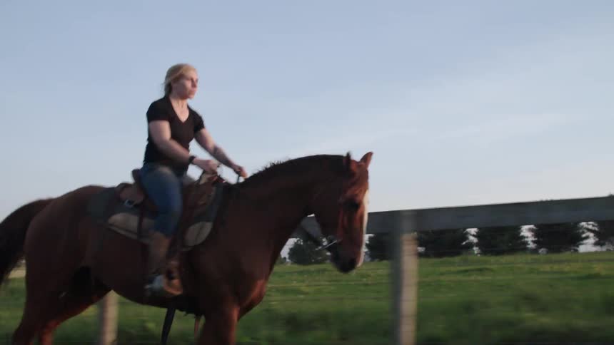 A woman is riding a horse near a wooden fence