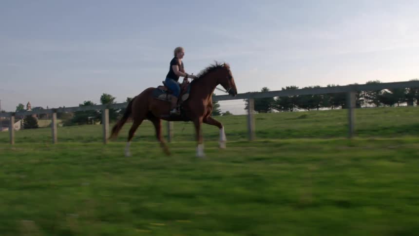 A woman is riding a horse over green grass