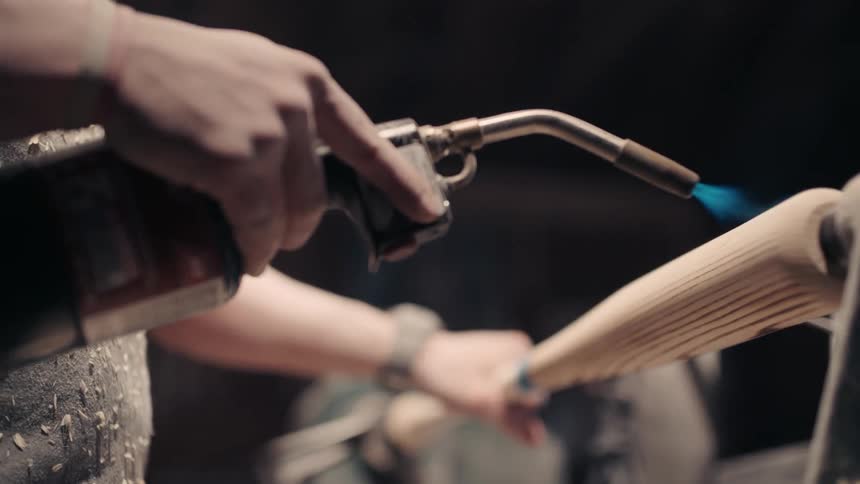 Person using a blowtorch to show wood grain in baseball bat