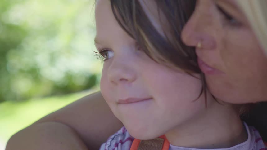 Mother holds child hugging and kissing outdoors in the middle of the day