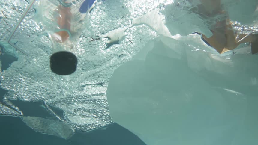 Underwater footage of plastic and varied garbage floating on the surface of the water