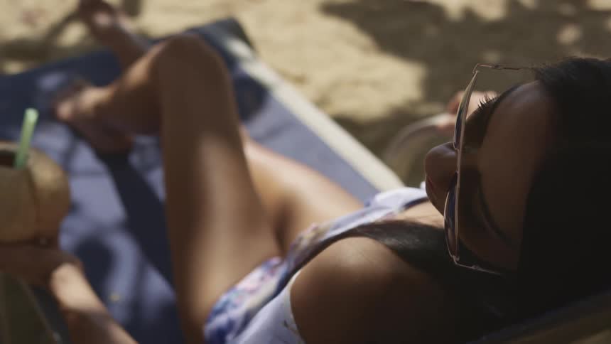 Young woman wearing sunglasses relaxing with a cocktail on a reclining chair on the beach
