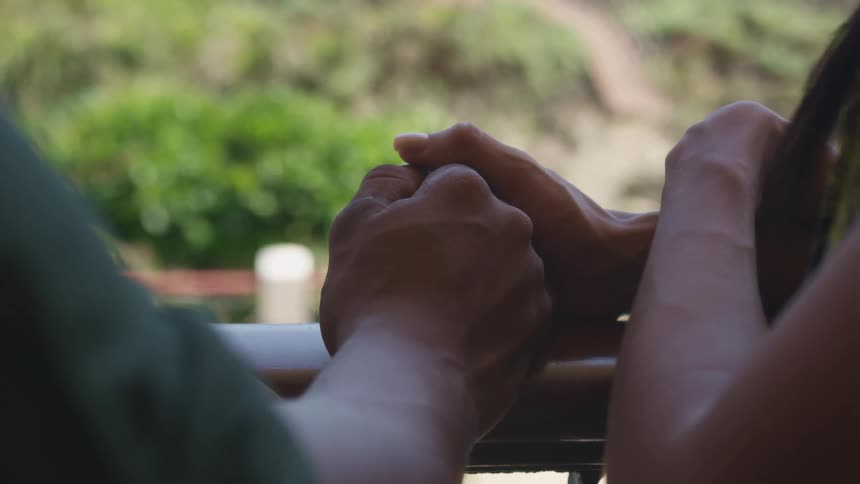 Man dand woman holding hands on the handrail of a porch looking outdoors