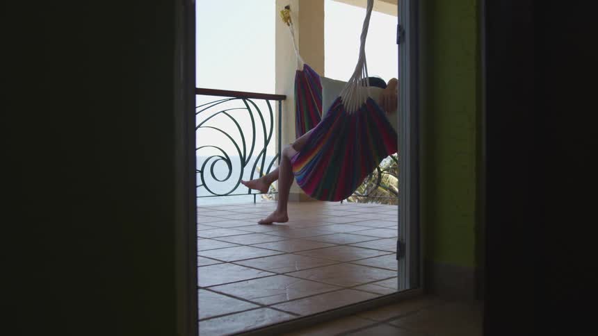 A person sits still on a hammock hung on an outside balcony