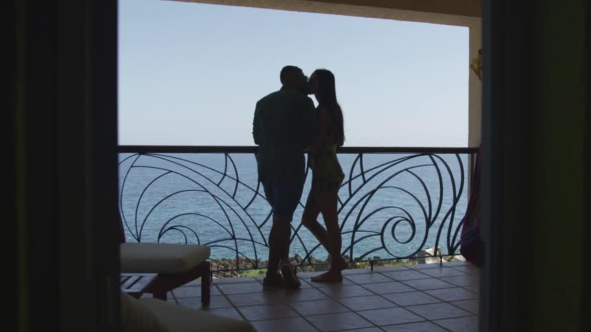 Young couple kissing reclined on a handrail in the balcony of a hotel near the ocean