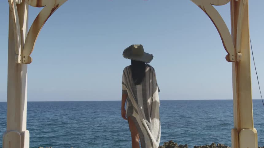 A woman wears a hat as she stands outdoors looking over the ocean