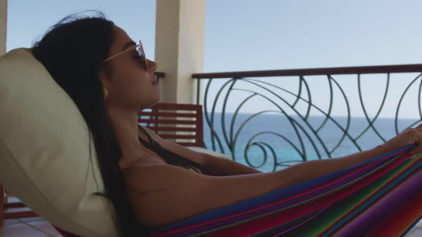 A woman relaxing in a hammock by an ocean