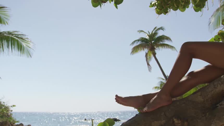 A woman is reclines on a tree trunk at the beach overlooking a sparkling ocean