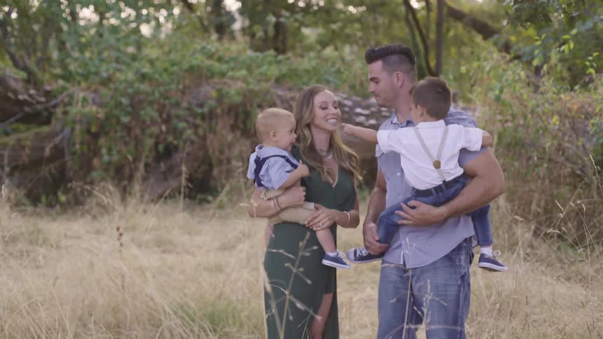 Young couple kiss while holding their babies on their arms outdoors at evening
