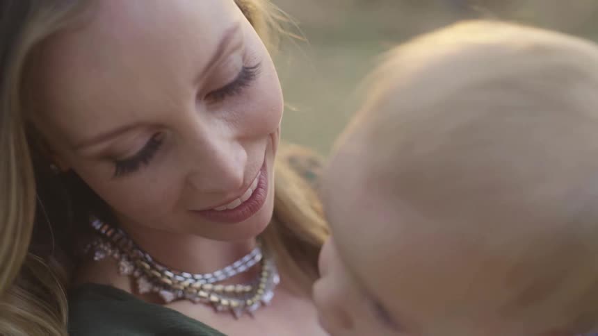Mother holding son in his hand while he looks at the camera smiling outdoors at sunset