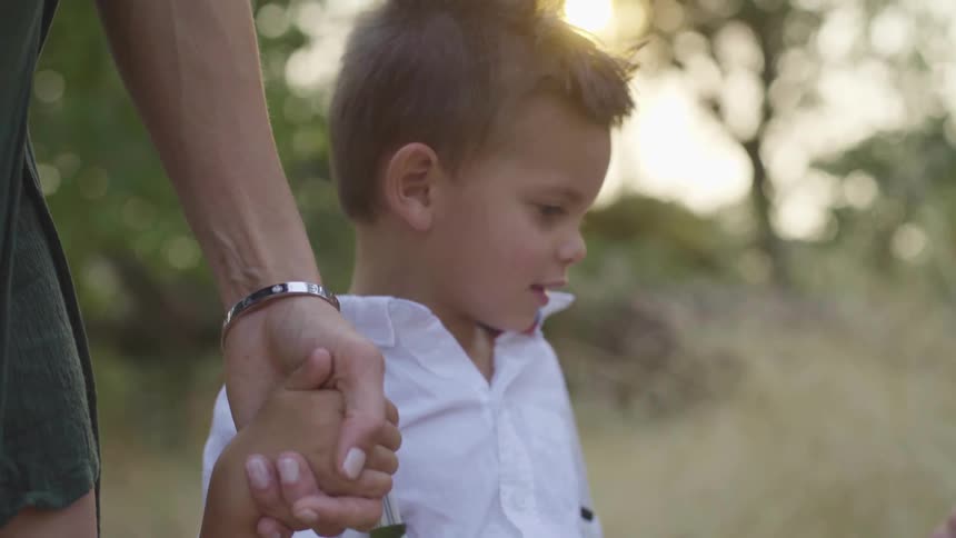 A young boy holds his mothers hand and touches his younger siblings head as they stand in a field