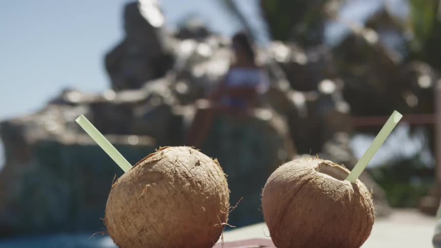Two coconut cocktail drinks on the bar in front of a girl relaxing on a cascade fountain