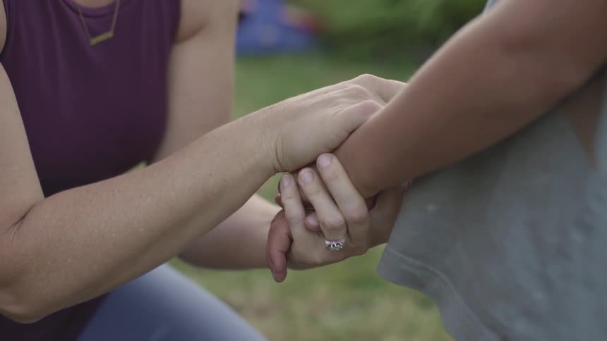 A woman kneeling down holds her sons hands as she talks with him