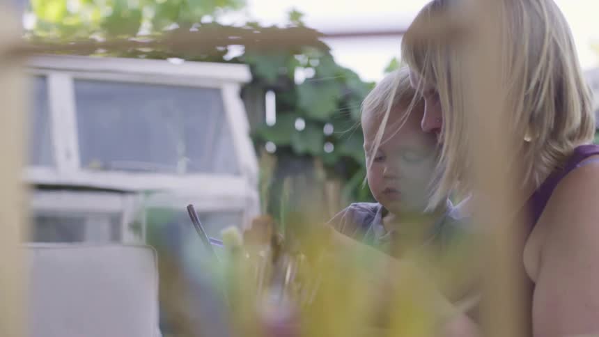 Mom and young son sit outside next to a boat gathering paint brushes
