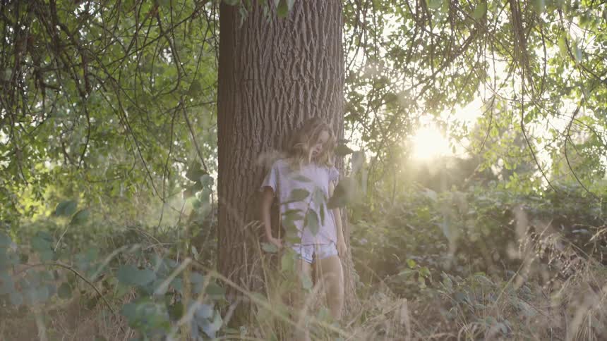 Girl leaning against a large tree in the woods with the sun shining through the branches