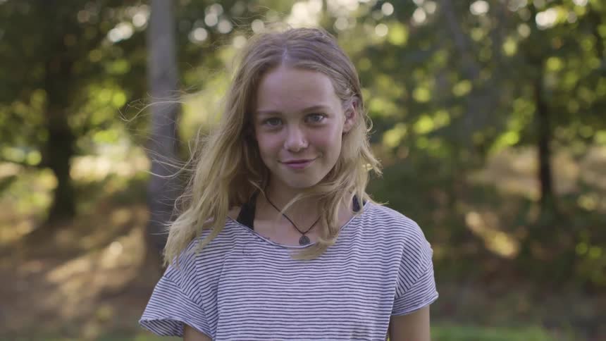 A young girl smiles as she stands in front of trees in a forest
